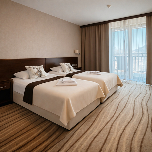 Pokój z dwoma pojedynczymi łóżkami, pościel, ozdobne poduszki, złożone ręczniki, ciemne meble, biurko i balkon z widokiem.