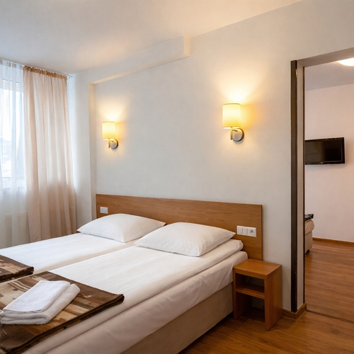 Jasny pokój dwuosobowy z dwoma łóżkami, białą pościelą, kocami i ręcznikami, drewnianym zagłówkiem, kinkietami i zasłonami.