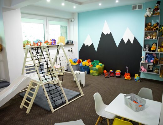 Przytulny hotelowy kącik zabaw: zjeżdżalnia i ścianka do wspinaczki, stolik z krzesełkami, kosze klocków i pluszaki