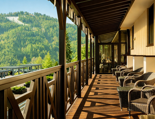 Drewniany hotelowy taras z wiklinowymi fotelami, porannym słońcem i widokiem na zalesione górskie stoki