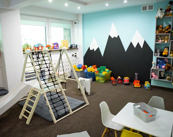 Przytulny hotelowy kącik zabaw: zjeżdżalnia i ścianka do wspinaczki, stolik z krzesełkami, kosze klocków i pluszaki