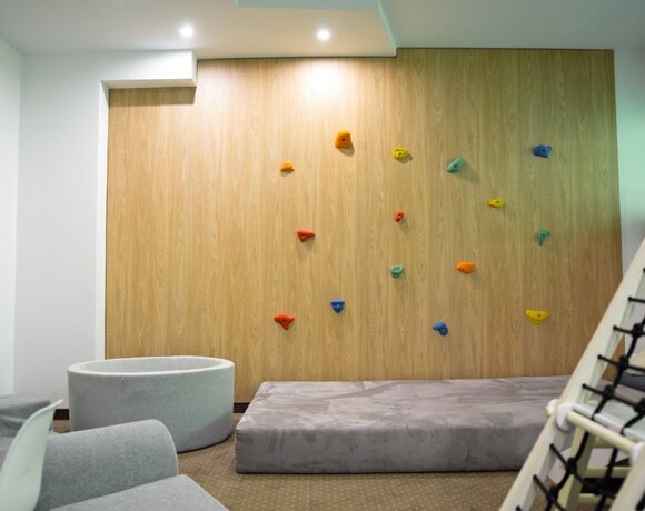Hotelowy, przyjazny kącik rodzinny z niską ścianą wspinaczkową, kolorowymi chwytami, miękkimi materacami i siedziskami