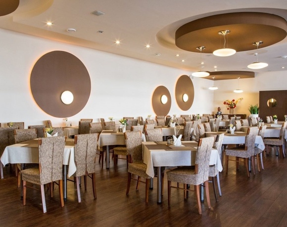 Przestronna restauracja hotelowa z nakrytymi stolikami, lnianymi obrusami, wygodnymi krzesłami, okrągłymi lampami i kwiatami.