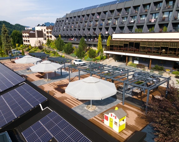 Hotel z tarasem z pergolami i dużymi parasolami, leżakami, przeszkloną restauracją, panelami słonecznymi i górskim widokiem