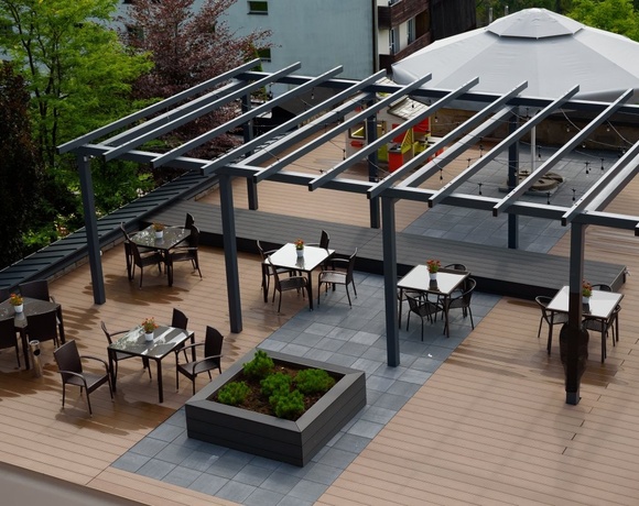 Taras na dachu z pergolą, drewnianą podłogą, stolikami i krzesłami z kwiatami, dużym parasolem i delikatnym oświetleniem