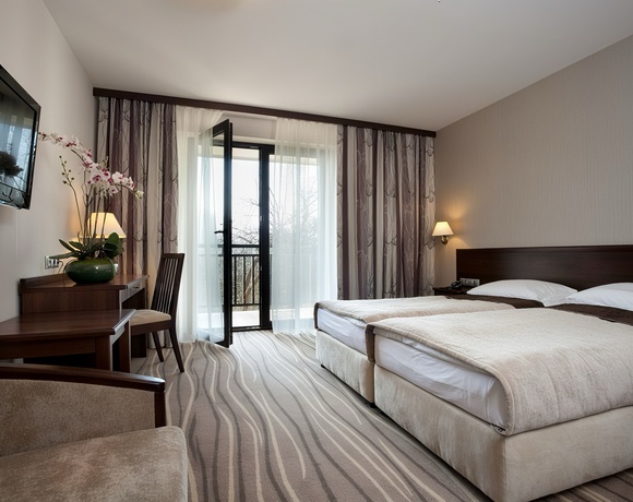 Elegancki pokój z dwoma pojedynczymi łóżkami, balkonem przez przeszklone drzwi, biurkiem z orchideą, telewizorem i lampami nocnymi.