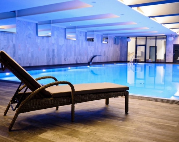 Leżak przy krytym basenie spa hotelowego, niebieskie nastrojowe oświetlenie, nowoczesne płytki i relaksująca atmosfera