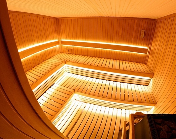 Przestronna drewniana sauna hotelowa z wielopoziomowymi ławkami, podświetleniem LED i piecem z kamieniami