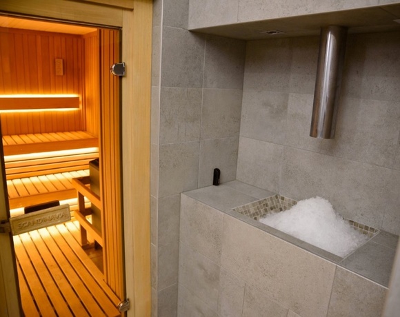 Sauna z drewnianymi ławami i ciepłym podświetleniem oraz przylegający pojemnik z kruszonym lodem i stalową rurą