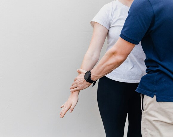 Trener rozciąga przedramię kobiety — intymna sesja wellness/terapia manualna, skupiona na mobilności ramienia