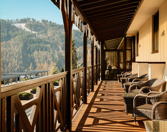 Balkon hotelowy z rattanowymi fotelami, drewnianą balustradą, zalegającymi soplami lodu i widokiem na ośnieżone góry