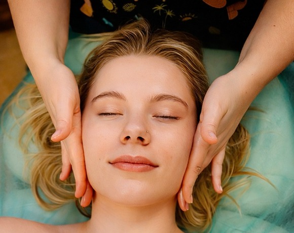 Kobieta z zamkniętymi oczami podczas relaksującego masażu twarzy w pokoju spa, na leżance z białym ręcznikiem