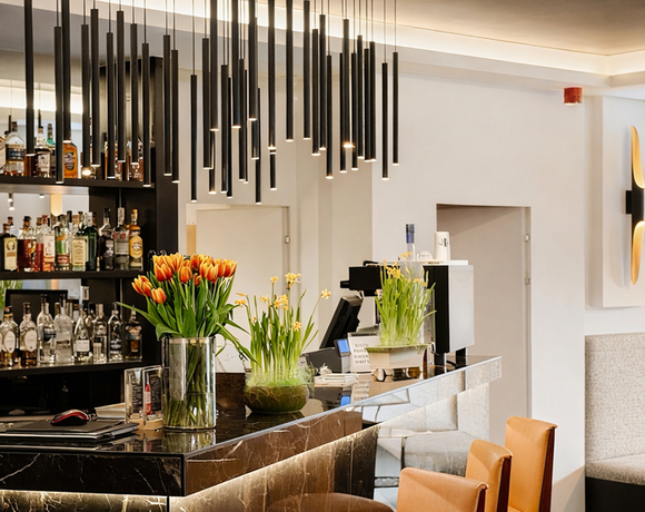 Elegancki bar z czarnym marmurowym blatem, wiszącymi rurkowymi lampami, skórzanymi stołkami i bukietami tulipanów.