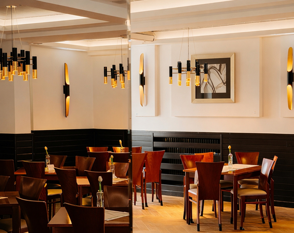 Restauracja hotelowa z drewnianymi stołami i krzesłami, ciepłym zwisającym oświetleniem, lustrzaną ścianą i pojedynczymi kwiatami na stołach