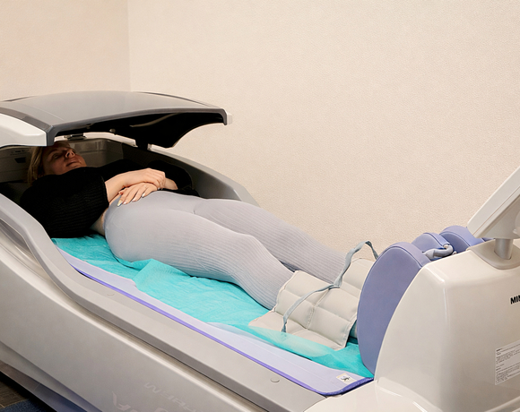 Gość leżący w nowoczesnej kapsule spa z kompresją nóg, miękkim materacem i łagodnym, relaksującym wnętrzem.