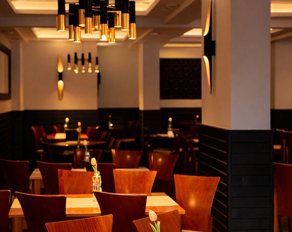 Elegancka, przytulna restauracja hotelowa z drewnianymi stolikami, pojedynczymi tulipanami, złotymi zwisającymi lampami i intymną atmosferą.