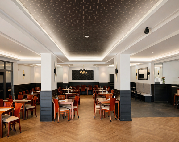 Przestronna restauracja hotelowa z dębową podłogą jodełką, drewnianymi stolikami, eleganckim kasetonowym sufitem i barem