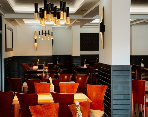 Elegancka restauracja hotelowa z drewnianymi stołami i krzesłami, złote wiszące lampy i pojedyncze tulipany w wazonikach.