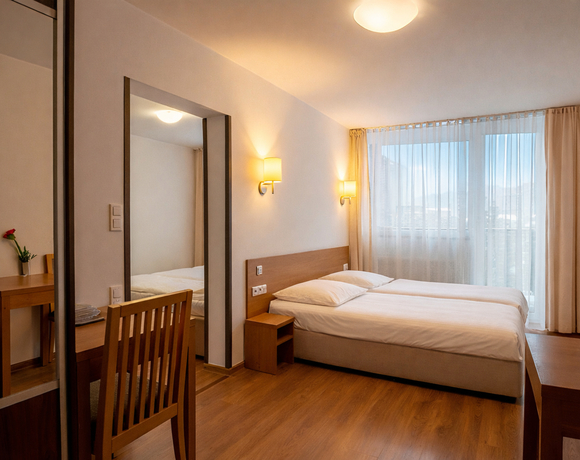 Jasny pokój hotelowy z dwoma łóżkami, drewnianymi meblami, biurkiem, telewizorem, kinkietami i przeszklonym balkonem z widokiem.