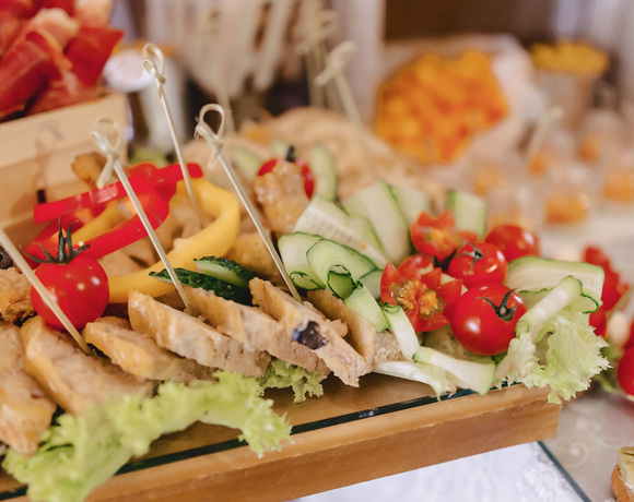Talerz bankietowych przystawek: plastry grillowanego kurczaka, ogórkowe wstążki, pomidorki koktajlowe i papryka na wykałaczkach