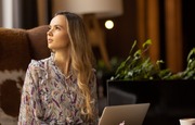 Gość pracujący w przytulnym hotelowym lobby przy laptopie, na miękkim fotelu z kawą obok, ciepłe oświetlenie, drewniane akcenty i rośliny