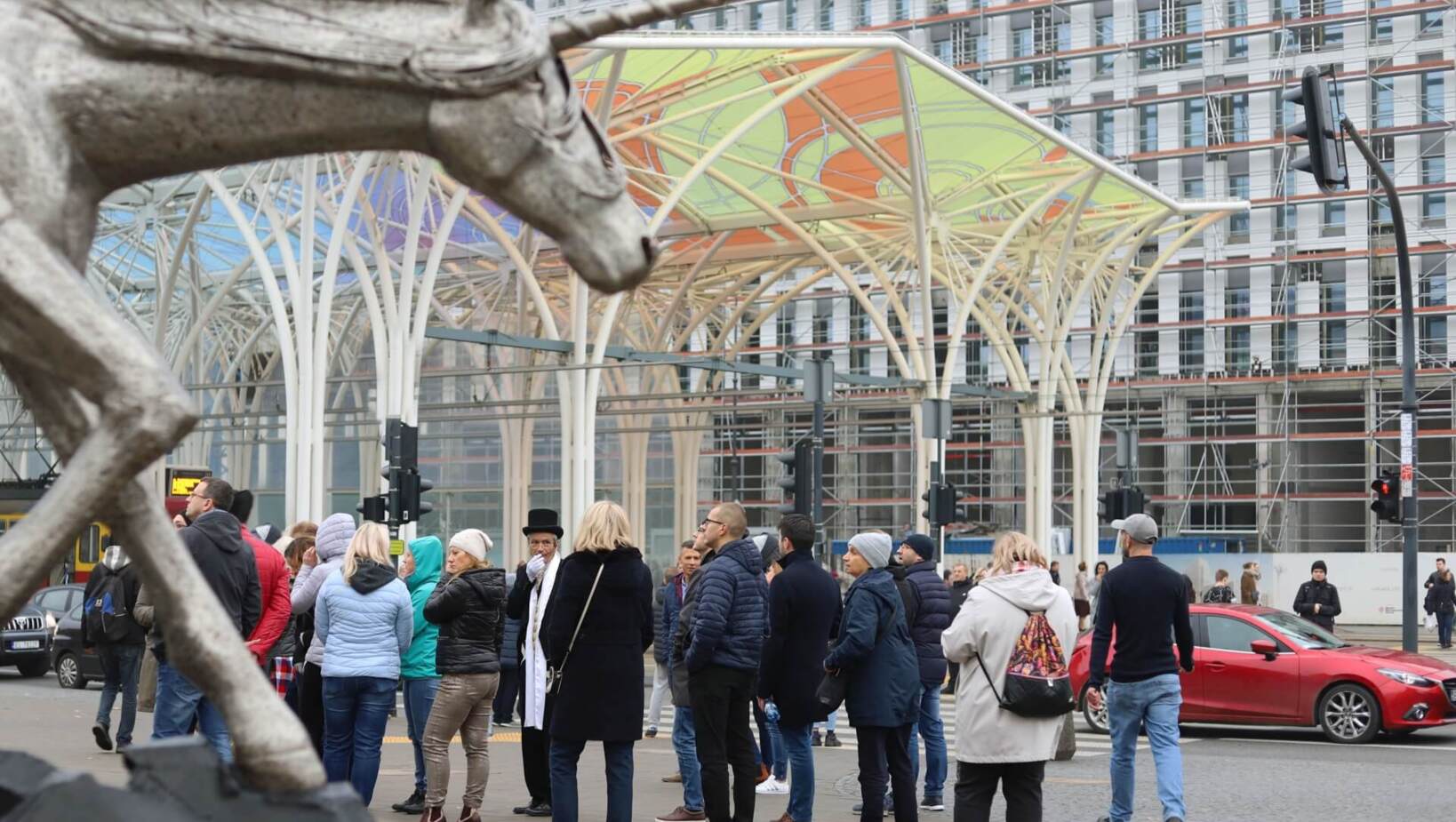 Group of people sightseeing Łódź, metal unicorn in the foreground, depot in the background