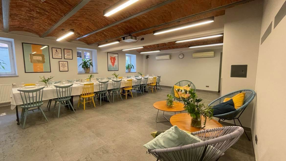 Duża sala z zastawionym stołem pod ścianą oraz stolikiem z krzesłem i poduszką w rogu