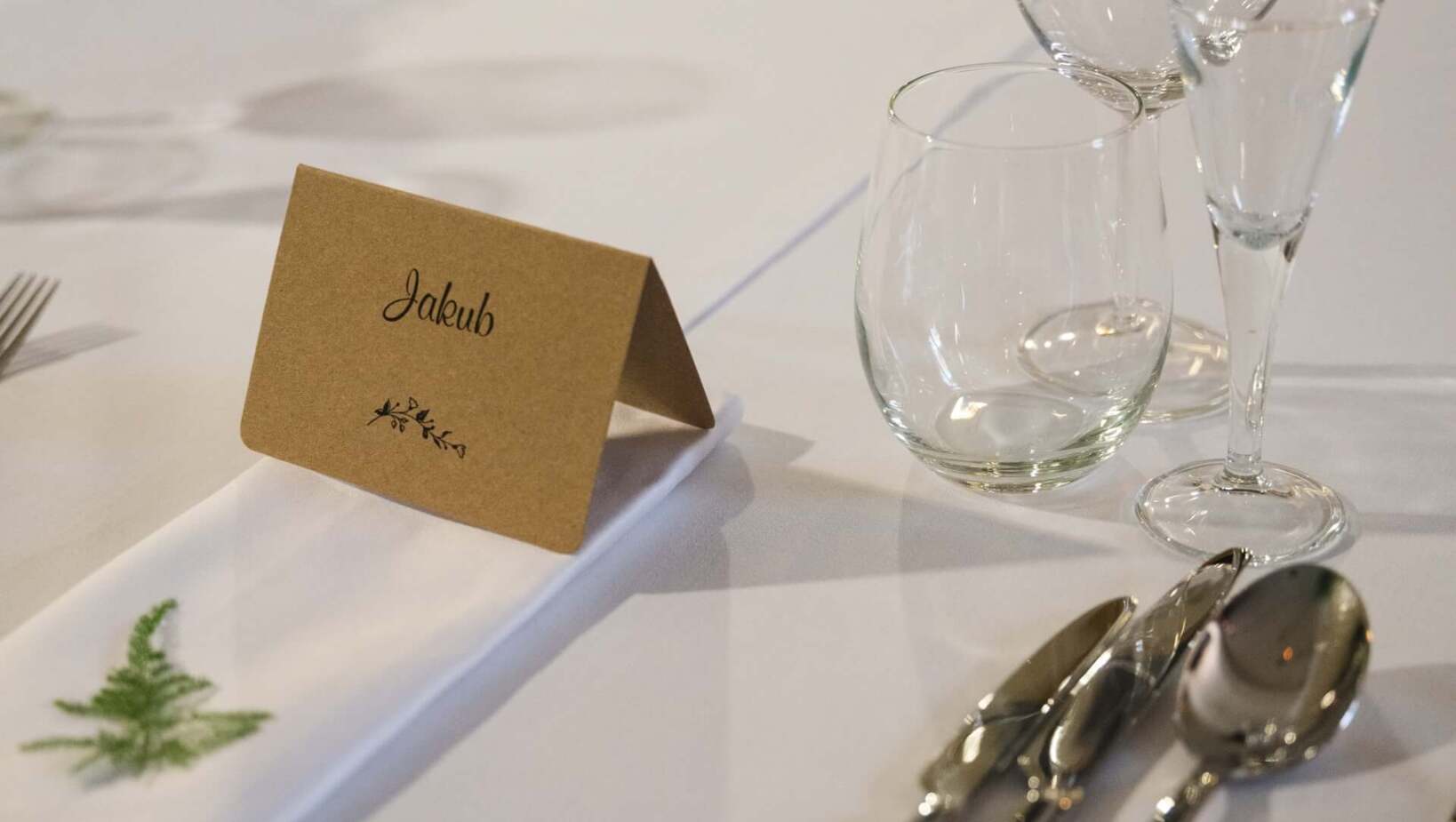 Imienna wizytówka na elegancko nakrytym stole obok sztućców i szklanek
