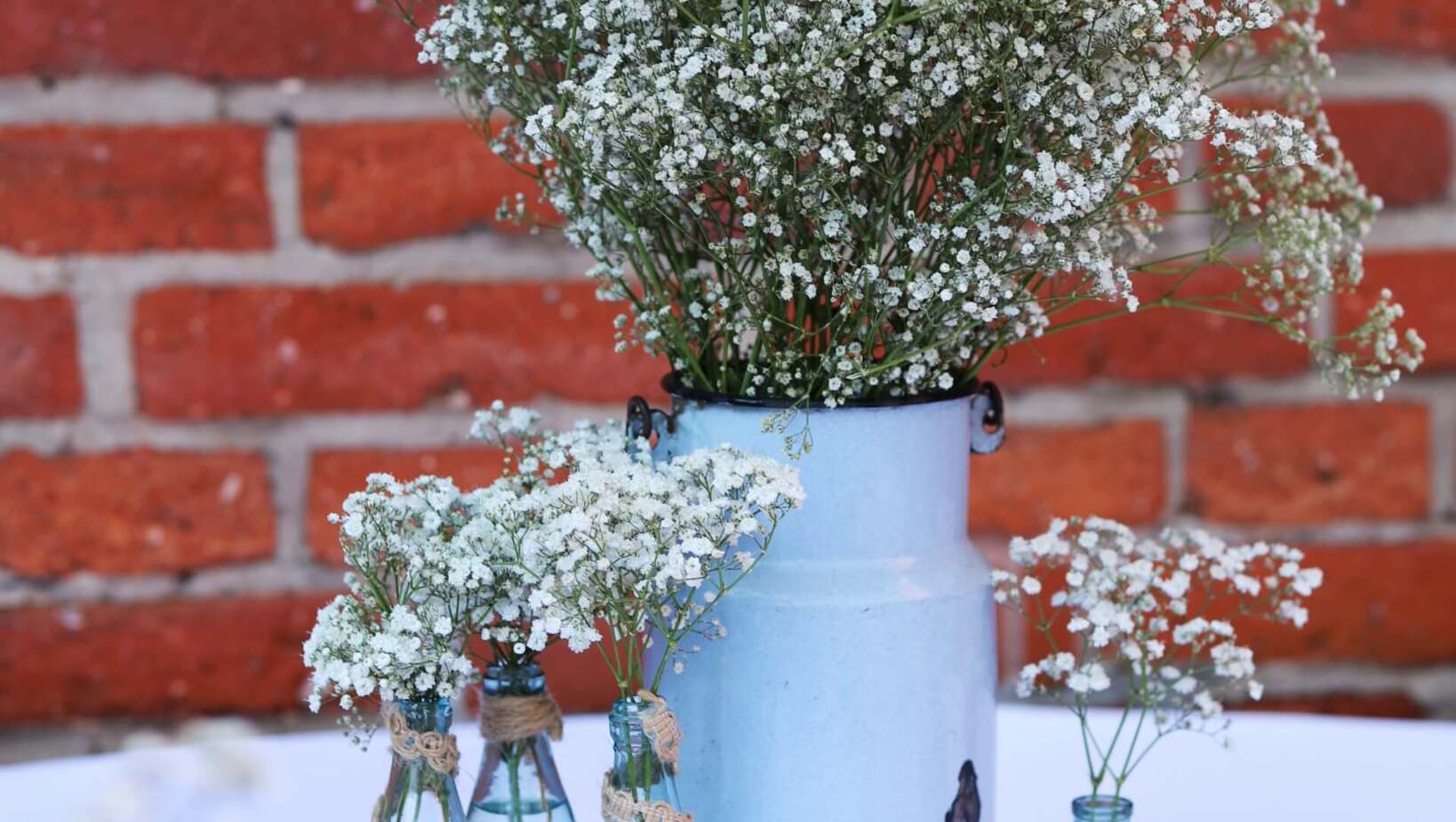 Bukiety z gipsówki przedstawiona w rustykalnym stylu we flakonach na stole, w tle ściana z cegły