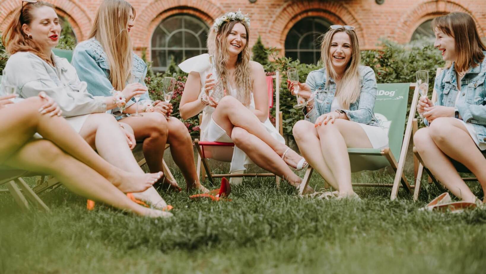 Friends on deck chairs in front of the hotel on the grass during bachelorette party with champagne
