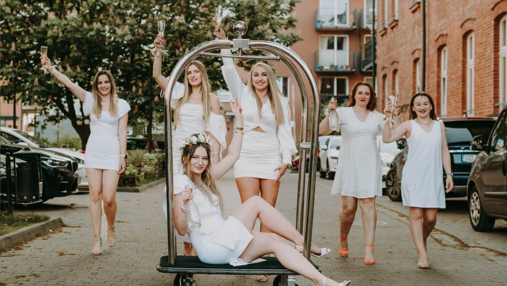 Group of friends dressed in white on hotel luggage cart celebrating bachelorette party