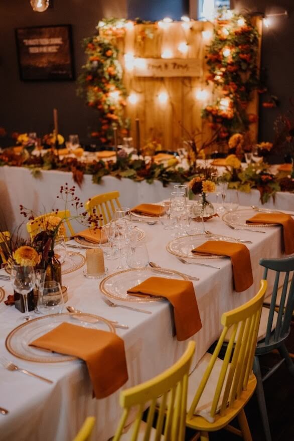Elegancko nakryte stoły z pomarańczowymi dekoracjami, w tle stół państwa młodych i świecące lampiony