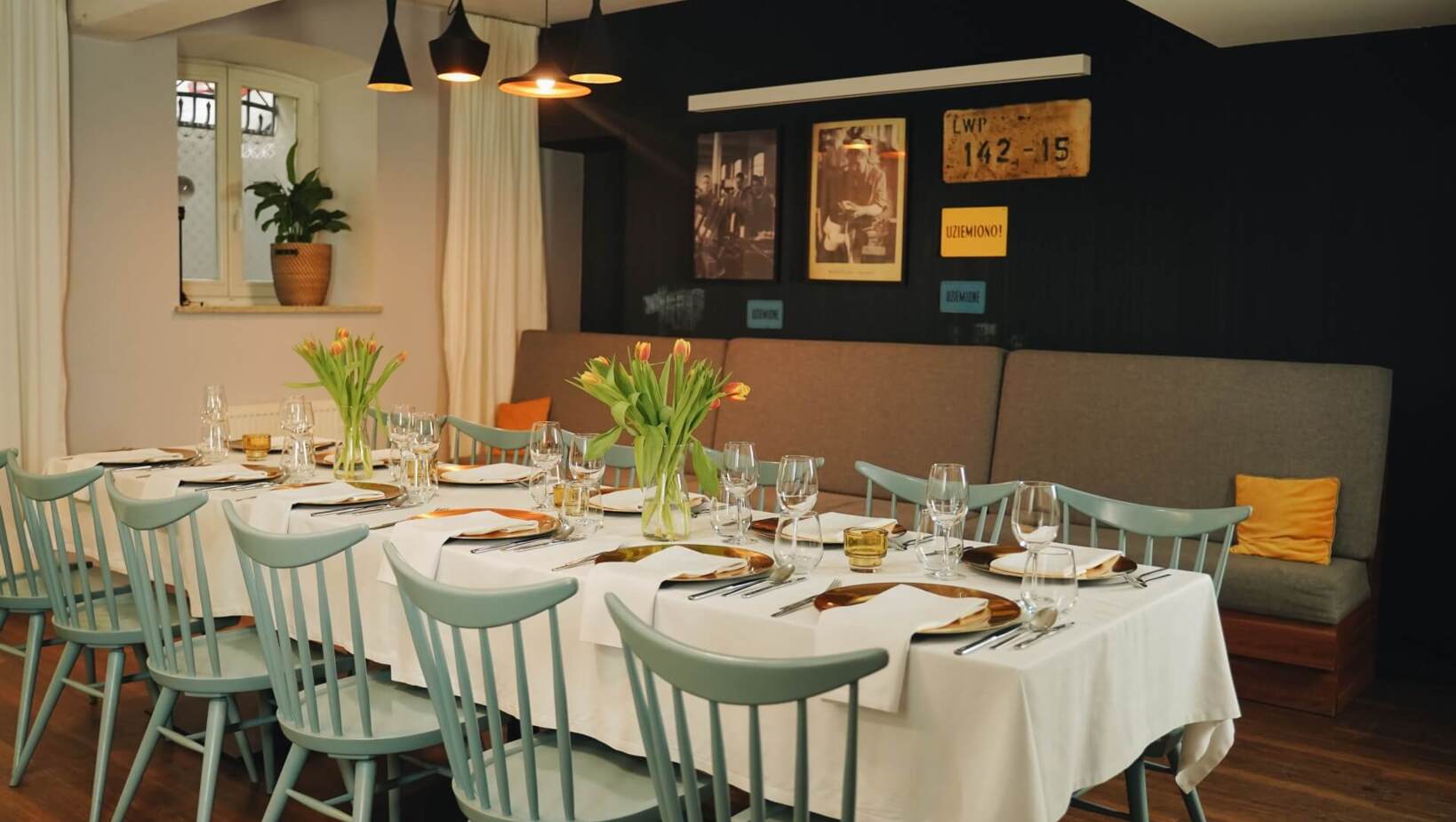 Pastelowe krzesła restauracyjne przy jasno zastawionym podłużnym stole oraz wygodna sofa