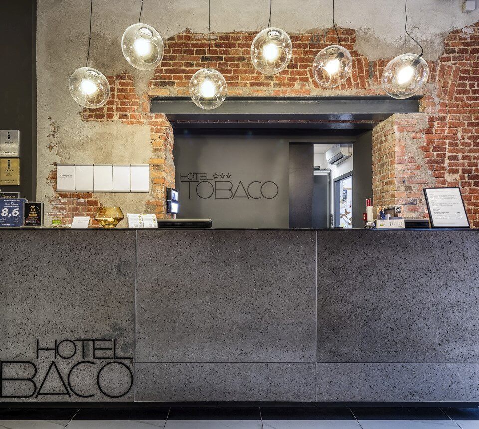 Lobby recepcji hotelu z industrialnym wystrojem, oświetleniem i charakterystyczną ceglaną ścianą