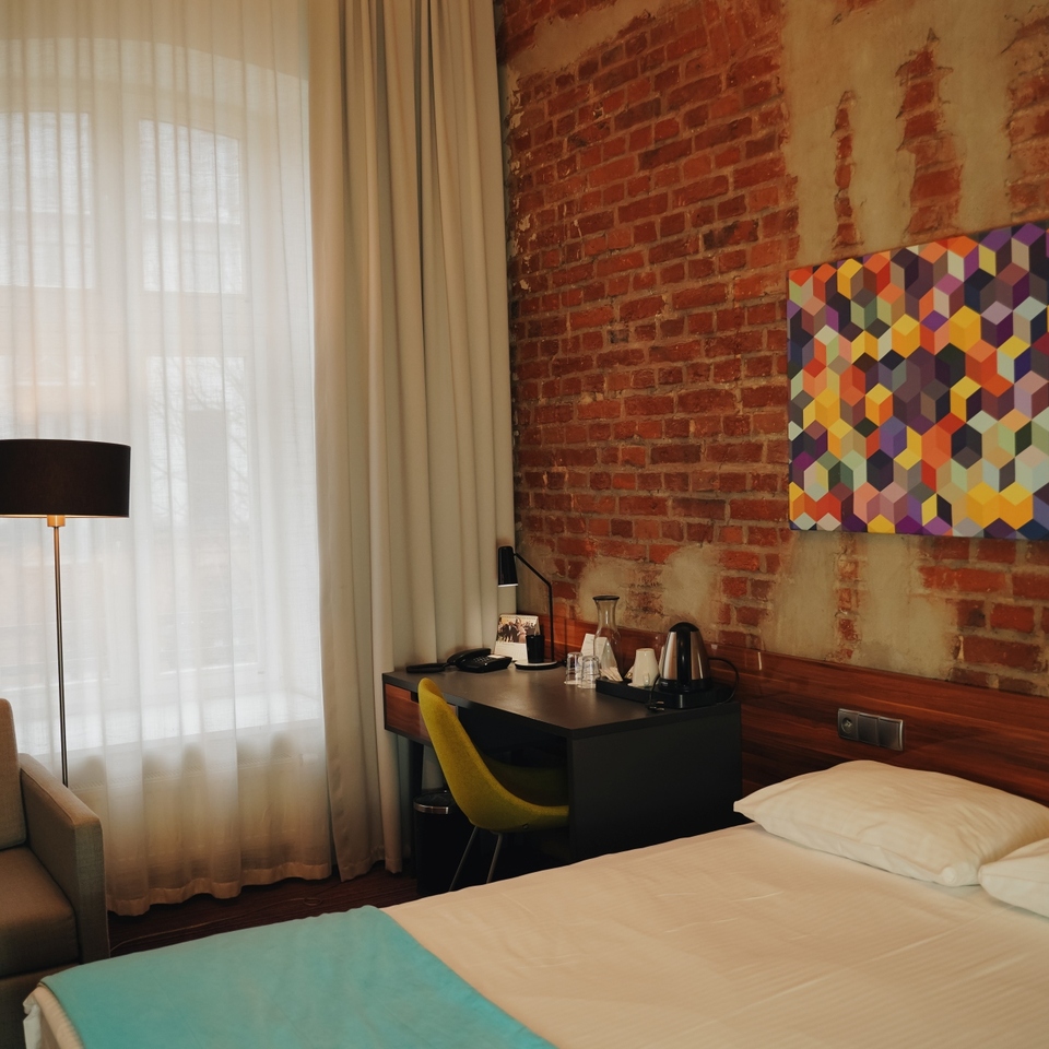 Nowoczesny pokój hotelowy Hotelu Tobaco w Łodzi z ceglanym murem, kolorową grafiką, biurkiem i sofą.