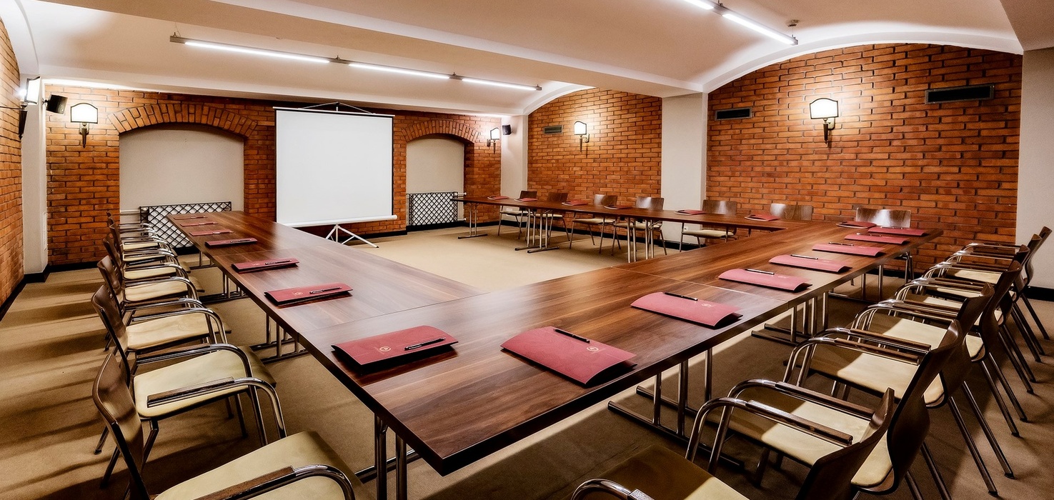 U-shaped meeting room with wooden tables, leather chairs, projector screen and warm exposed-brick walls