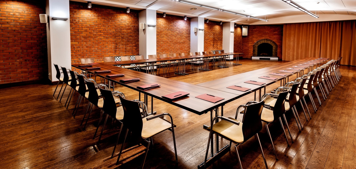 U-shaped conference room with wooden tables and chairs, warm brick walls, fireplace, hardwood floor and notepads ready for meetings