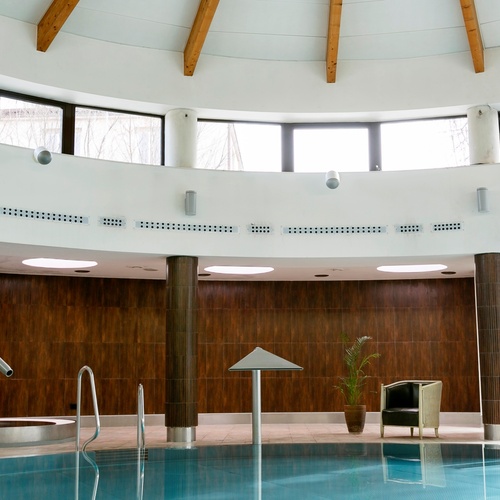 Vnitřní hotelové spa s kruhovým světlíkem, dřevěnými trámy, vířivkou a velkými okny od podlahy ke stropu