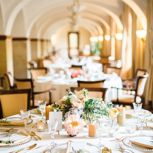 Elegant banquet dining room with arched ceilings, white-linen table set with floral centerpiece, candles, gold cutlery and crystal glassware.