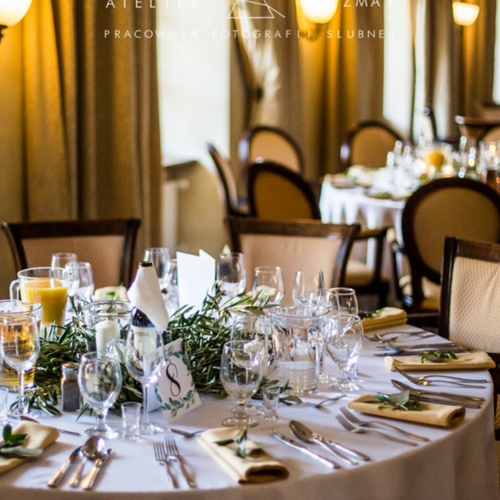 Elegantní banketová místnost s kulatými stolky na svatbu – bílé ubrusy, zelené dekorace, svíčky, sklenice, teplé osvětlení