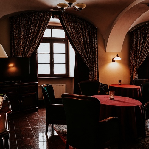 Cozy hotel lounge with arched ceilings, velvet armchairs, round tables with burgundy cloths, warm lamps and patterned drapes
