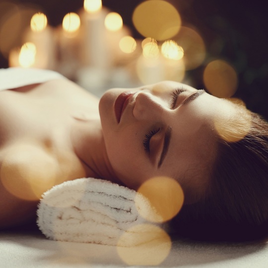 Kobieta relaksuje się podczas zabiegu spa, oczy zamknięte na zrolowanym ręczniku, ciepłe światło świec