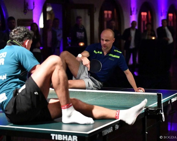 Evening hotel event with two men playing table tennis at a table in an elegant room, purple uplighting and guests watching
