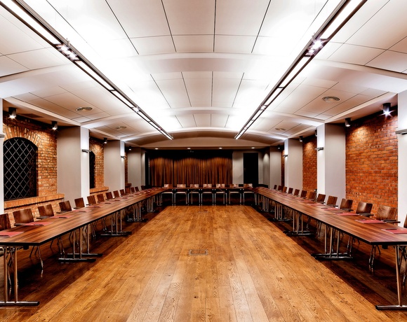 Geräumiger Konferenzraum in U‑Form mit langen Holztischen, Lederstühlen, freigelegten Backsteinwänden und warmem Licht