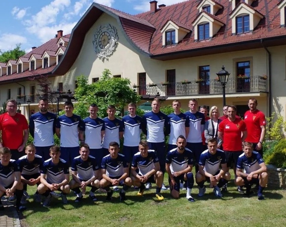 Football team and coaches posing on hotel lawn before a traditional gabled building with balcony, clock and gardens