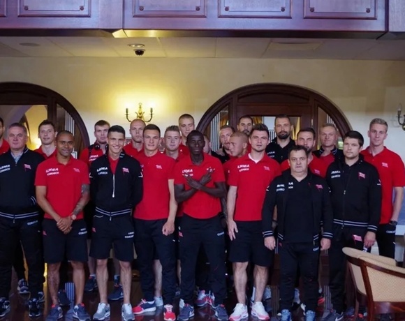 Team of men in red and black uniforms posing in a hotel lobby with wooden archways, wall sconces and lounge chairs