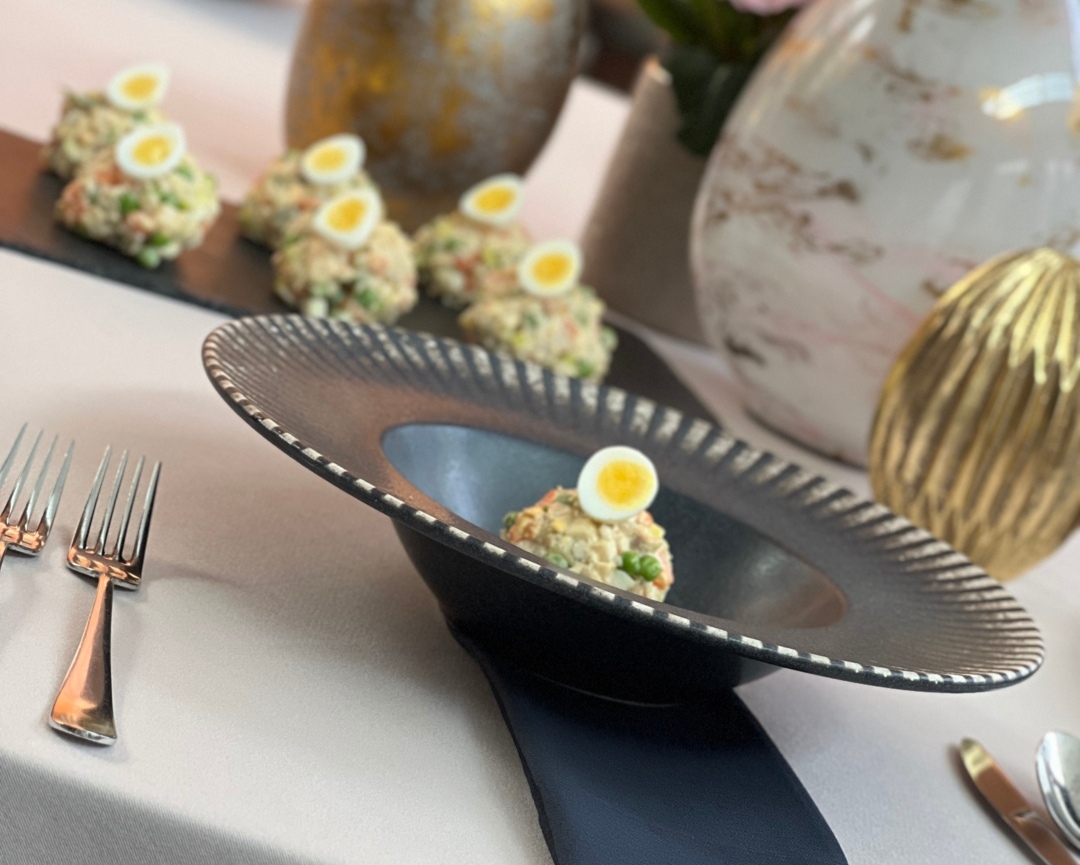 Elegancka przystawka: sałatka z połówką jajka przepiórczego w czarnej ozdobnej misie, białe obrusy i złote wazony.