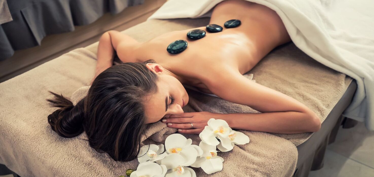 Kobieta relaksująca się podczas masażu gorącymi kamieniami w spa, z dekoracyjnymi białymi kwiatami na łóżku