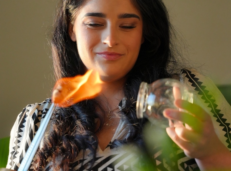 Kobieta zapalająca świecę w przytulnym, naturalnym otoczeniu, tworząca relaksującą atmosferę