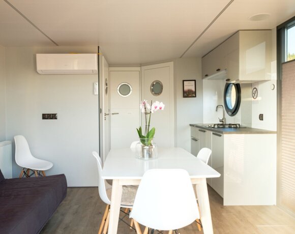 Nowoczesny, jasny apartament z kuchnią, białym stołem jadalnym na cztery osoby i okrągłymi oknami.